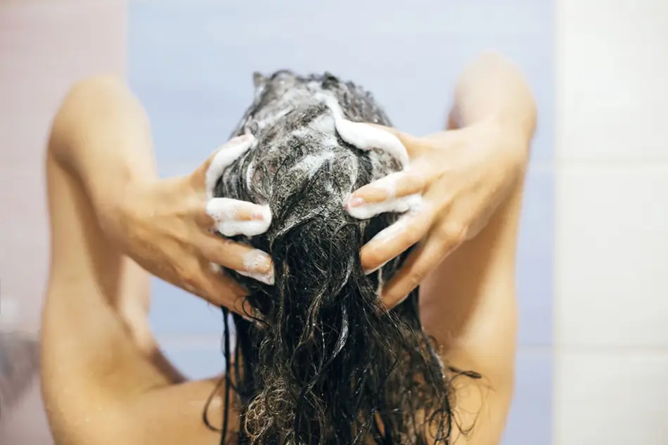 Comment choisir le bon shampoing pour cheveux frisés ? Femme se l.avant les cheveux avec un shampoing pour cheveux frisés