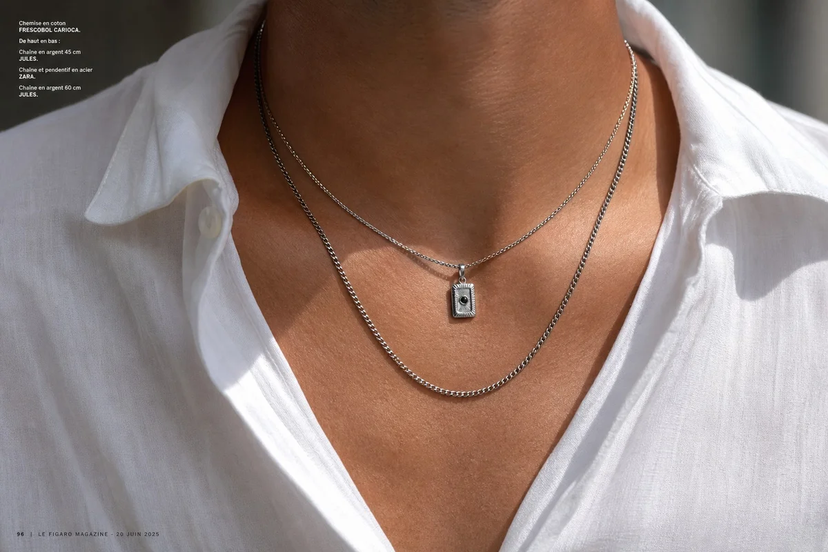 Layering colliers homme : superposer plusieurs chaînes de longueurs différentes Homme portant trois colliers superposés en acier et argent, layering tendance 2026
