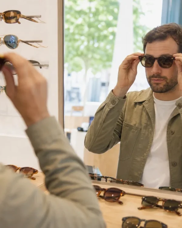 Homme essayant plusieurs paires de lunettes de soleil devant un miroir chez un opticien