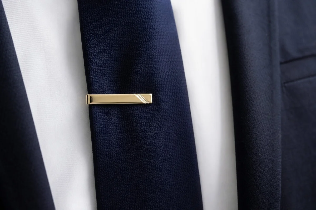 Pince à cravate positionnée entre le troisième et quatrième bouton de chemise Pince à cravate dorée fixée sur une cravate bleue au niveau du buste